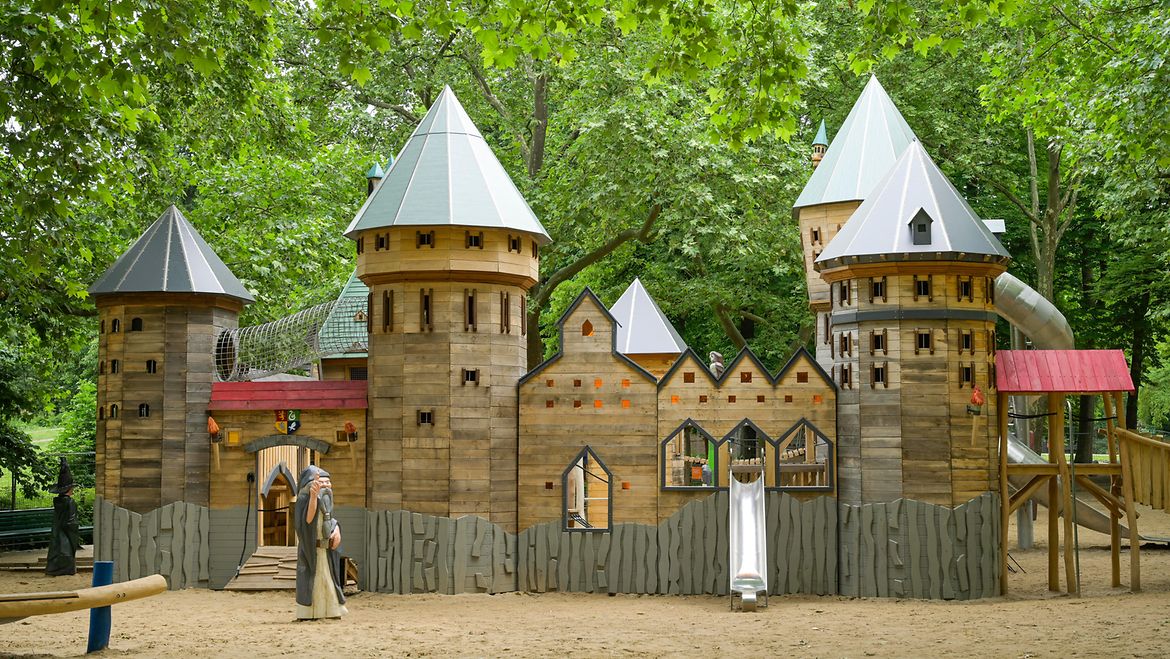 Das im Mai 2024 vollendete Projekt „Zauberspielplatz“ im Volkspark Wilmersdorf steht beispielhaft für die Beteiligung junger Menschen durch das Kinder- und Jugendparlament Charlottenburg-Wilmersdorf. Eine Zaubererfigur steht vor einem Spielplatz in Form einer Burg.