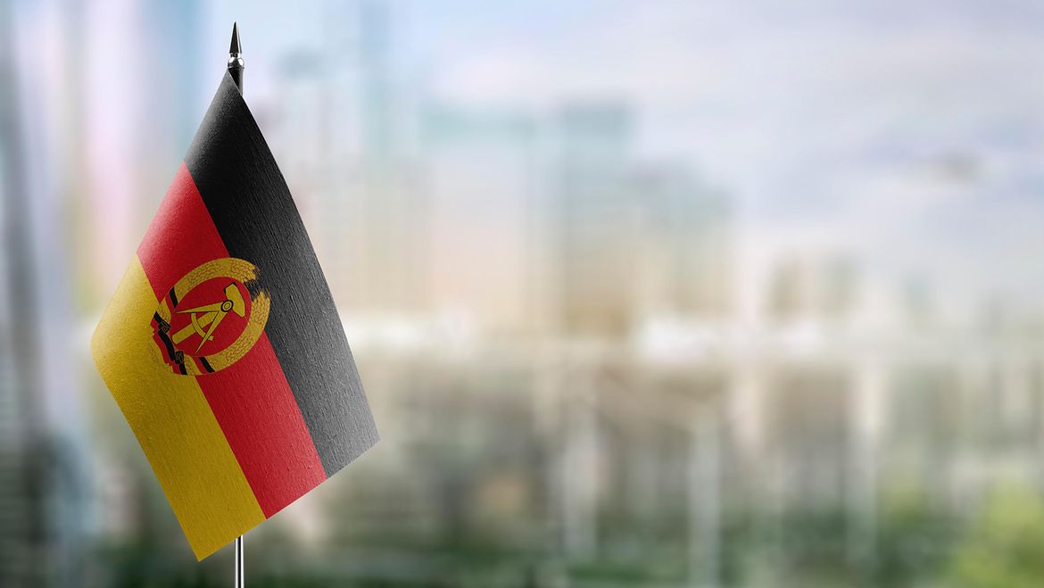 The black, red and gold flag of the GDR bearing the state emblem of a hammer and a pair of compasses inside a wreath of wheat ears. The black, red and gold flag of the GDR bearing the state emblem of a hammer and a pair of compasses inside a wreath of wheat ears.