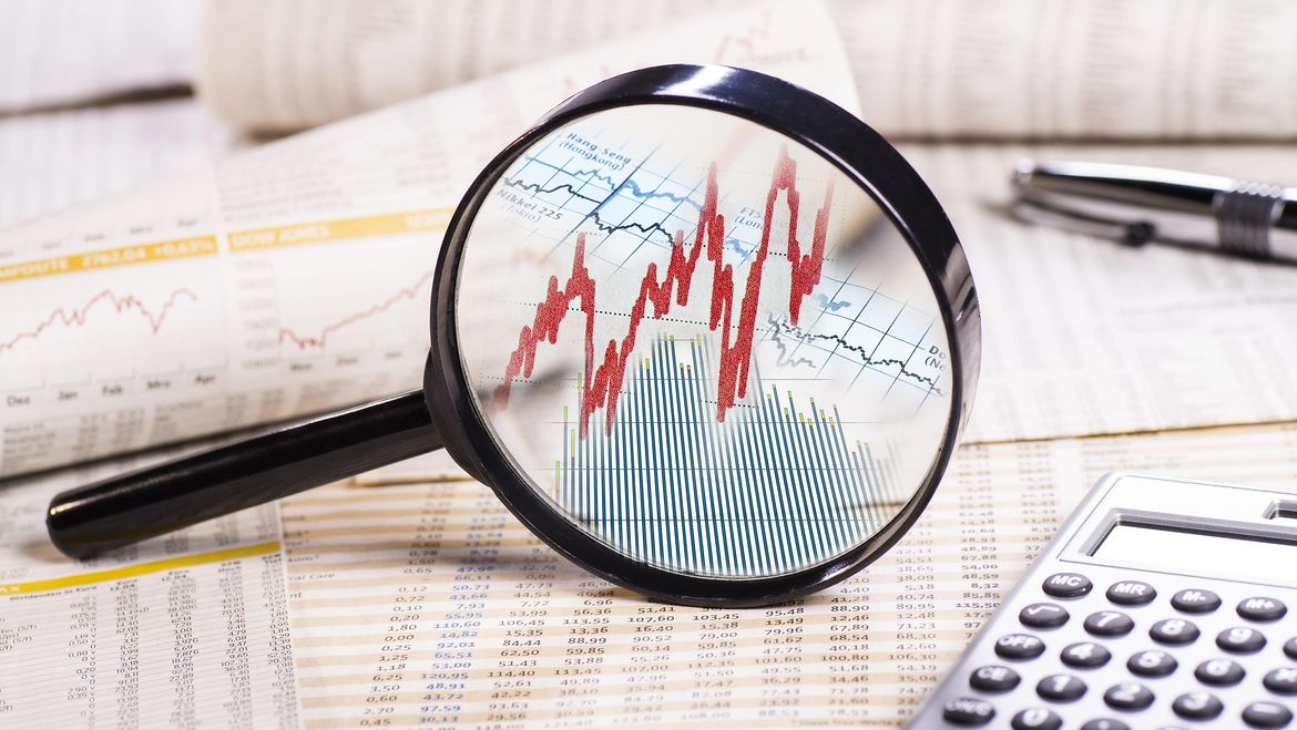 Lupe mit Aktienkursen auf Papieren mit Kurstabelle