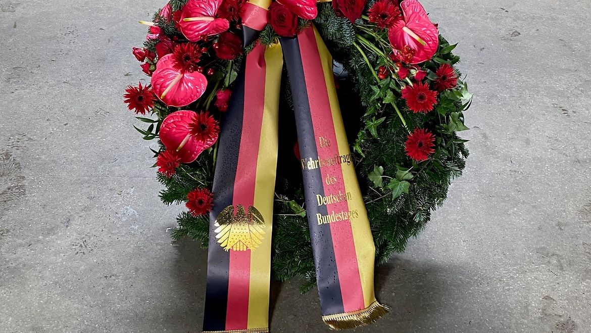 An einem Trauerkranz hängen Bänder in den Farben der Deutschlandfahne.